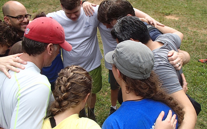 A group of people stand in a circle with their arms around each other's shoulders.